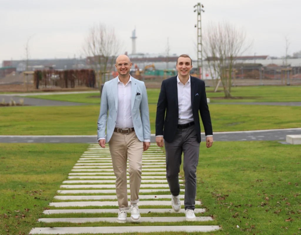 Zwei Männer spazieren auf einem gepflasterten Weg in einem Park, umgeben von kahlen Bäumen.